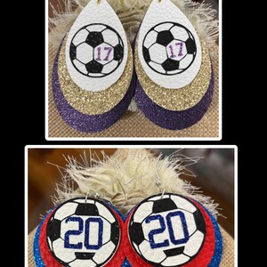 May include: Earrings with a soccer ball design. The top pair is teardrop-shaped with white, gold, and purple layers. The soccer ball has the number 17 in purple. The bottom pair is round with a soccer ball design and the number 20 in blue, with red and blue glitter layers.