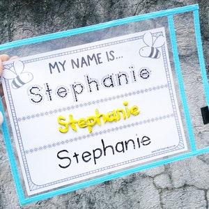 May include: A white sheet with a blue border and the words "My Name Is..." printed at the top. The name "Stephanie" is written three times in different ways: with dotted lines, with yellow foam letters, and in black marker.