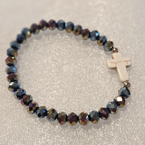 May include: A bracelet made of iridescent, faceted beads in blue, purple, and gold. It features a white cross charm and small gold-coloured beads. The bracelet is designed to be worn around the wrist.