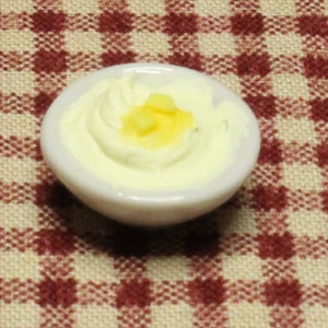 May include: A white ceramic bowl filled with a creamy white mashed potato topping with small pieces of yellow butter.