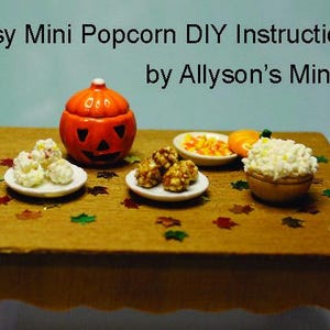 May include: A miniature wooden table featuring the text Easy Mini Popcorn DIY Instructions by Allyson's Minis, displaying a small orange jack-o'-lantern, three white plates with miniature popcorn and candy corn, and scattered colorful leaf confetti.