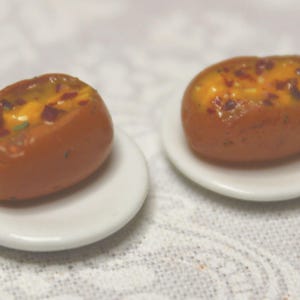 May include: Two miniature baked potatoes with a cheesy filling, topped with red and yellow ingredients. The potatoes are on small white plates.