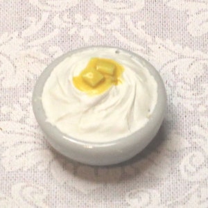 May include: A white bowl filled with mashed potatoes topped with a dollop of melted butter.