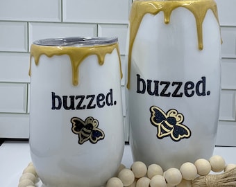 May include: Two white tumblers with gold dripping paint and a black bee graphic. The tumblers say "buzzed."