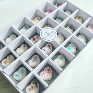 May include: A white box filled with 20 heart-shaped wax melts. The wax melts are decorated with colourful glitter. The box has a label that says "The Cottage Wax Melts".