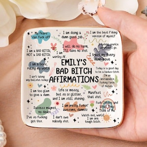 Könnte beinhalten: Ein quadratisches Keramiktablett in Weiß mit dem Text "Emily's Bad Bitch Affirmations" in Schwarz. Das Tablett hat verschiedene Affirmationen in schwarzem Text und florale Akzente. Das Tablett wird von einer Person gehalten.
