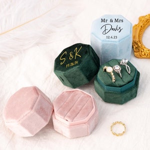 Peut inclure: Plusieurs boîtes à bagues en velours de différentes couleurs, dont rose, bleu sarcelle et vert. Certaines boîtes sont ouvertes, exposant des bagues. Les boîtes octogonales ont des textes personnalisés avec des initiales et des dates.