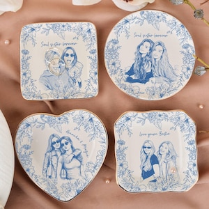 Könnte beinhalten: Vier Schmuckschalen aus Keramik in quadratischer, runder und herzförmiger Ausführung mit blauen Blumenrändern und Strichzeichnungen von zwei Personen. Die Schalen enthalten Texte wie Soul sister forever, Annika & Mazie und Love you're Bestie.
