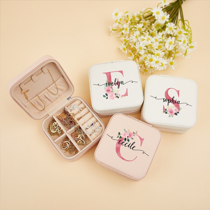 Pu&ograve; includere: Quattro scatole per gioielli rosa e bianche con motivi floreali e personalizzate con le lettere E, S e C. Le scatole sono aperte e chiuse, mostrando i scomparti interni e uno specchio.