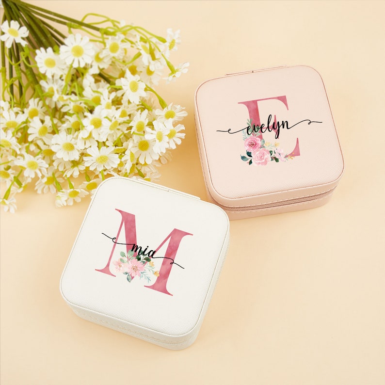 Pu&ograve; includere: Due scatole per gioielli quadrate con disegni floreali e iniziali personalizzate. La scatola a sinistra &egrave; bianca con l'iniziale "M" e il nome "mia" scritto in corsivo. La scatola a destra &egrave; rosa con l'iniziale "E" e il nome "evelyn" scritto in corsivo.