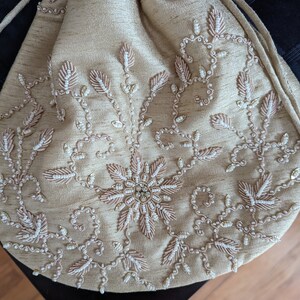 May include: A beige drawstring bag with intricate embroidery featuring a floral design with white and pink beads.