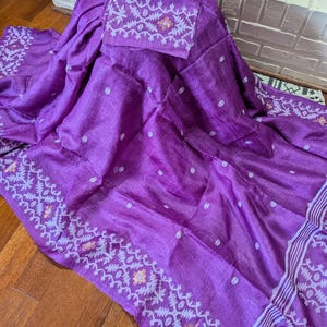 May include: A vibrant purple textile with a matching square piece, possibly a scarf or shawl. The fabric features a delicate pattern along the edges and on the square piece, with small white dots scattered across the main body. The textile is draped over a surface.