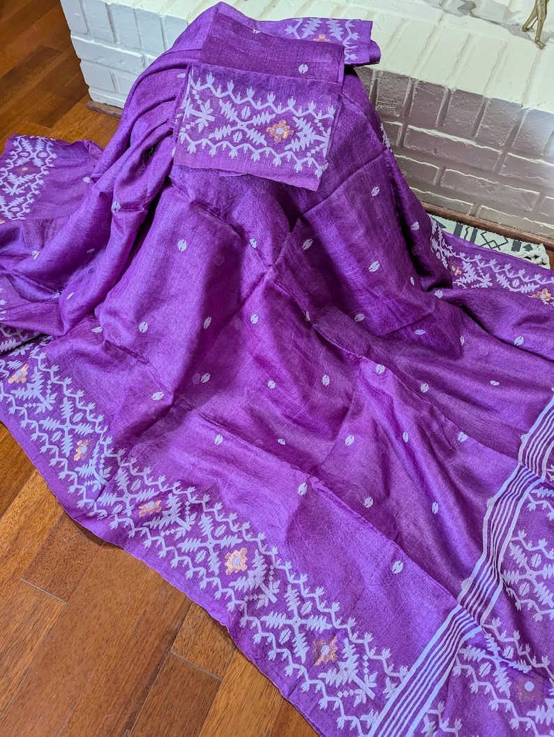 May include: A vibrant purple textile with a matching square piece, possibly a scarf or shawl. The fabric features a delicate pattern along the edges and on the square piece, with small white dots scattered across the main body. The textile is draped over a surface.
