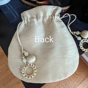 May include: A beige drawstring bag with a gold and white beaded tassel. The bag has the word "Back" written on it.