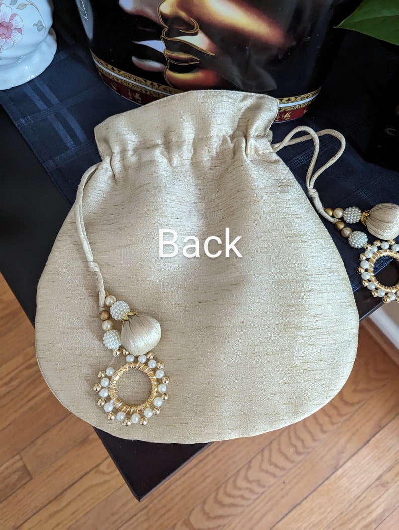 May include: A beige drawstring bag with a gold and white beaded tassel. The bag has the word "Back" written on it.