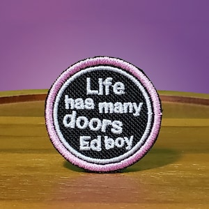 May include: A black and white embroidered patch with a pink border. The patch says "Life has many doors Ed boy".