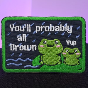 Può includere: Toppa ricamata verde con due rane e il testo "You'll probably all drown" e "Yup" in bianco.