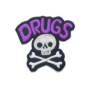 May include: Purple embroidered patch featuring the word "DRUGS" in a skull and crossbones design.