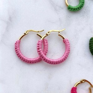 Może przedstawiać: Zestaw kolorowych kolczyków koła ze złotymi obręczami. Kolczyki wykonane są z plecionego sznurka w różnych kolorach, w tym niebieskim, zielonym, czerwonym i różowym.