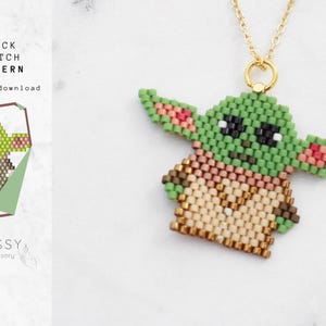 Op de afbeelding: Een groene en bruine kralenketting met een hanger in de vorm van een cartoonfiguur met grote oren. De hanger is gemaakt van kleine kralen in een baksteenpatroon. De ketting is gemaakt van gouden ketting.