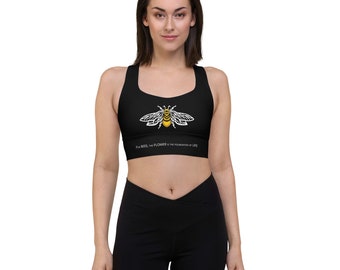 May include: Black sports bra with a bee graphic in yellow and white. The text "For bees, the flower is the foundation of life" is printed below the bee. The bra is worn with black leggings.