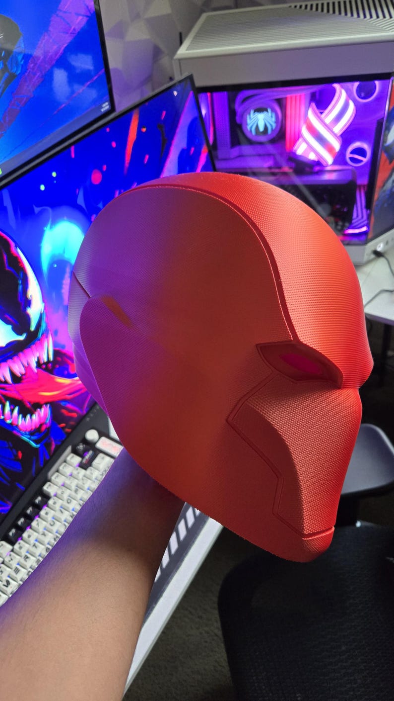 May include: A bright red, textured helmet, likely for cosplay or costume use. The helmet has a smooth, rounded design with defined facial features and a textured surface. The overall shape suggests a superhero or comic book theme.