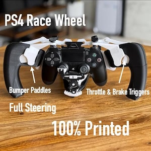 May include: A black and white 3D printed PS4 Race Wheel attachment for a game controller. It features white bumper paddles, throttle and brake triggers, and a central gear mechanism. The text PS4 Race Wheel, Bumper Paddles, Throttle & Brake Triggers, Full Steering, and 100% Printed are visible.