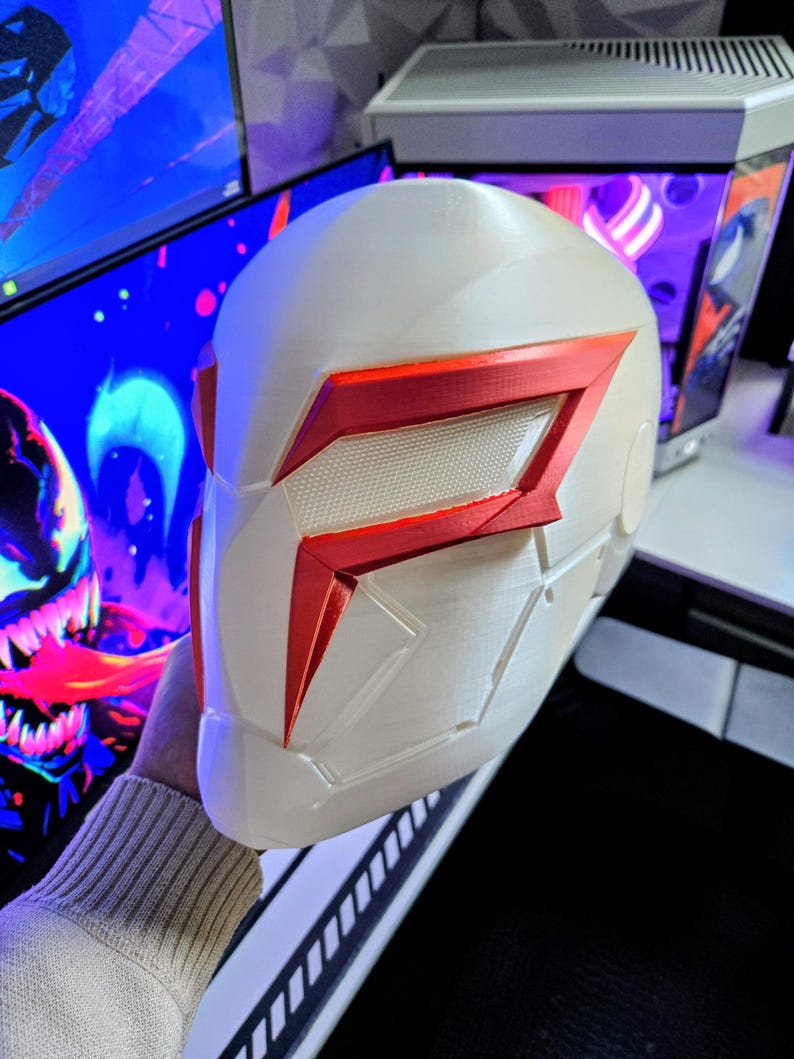 May include: A white and red helmet with a futuristic design. The helmet features a prominent red visor and accents, with a textured pattern on the visor. The overall aesthetic suggests a sci-fi or cosplay theme.