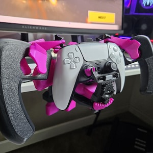 Op de afbeelding: Een gaming accessoire met een witte en zwarte PlayStation 5 controller geïntegreerd in een roze en zwart stuurwiel-achtig frame. Het heeft een tandwielmechanisme, ontworpen voor verbeterde gamebesturing.