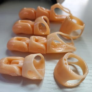 May include: A set of seven beige plastic fingertip protectors with different shapes and sizes. The protectors are designed to protect fingertips from injury.