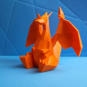 May include: An orange, geometric dragon figurine with outstretched wings and a seated pose. The dragon is made of angular, flat planes, giving it a modern, stylized look. The background is a textured blue surface.