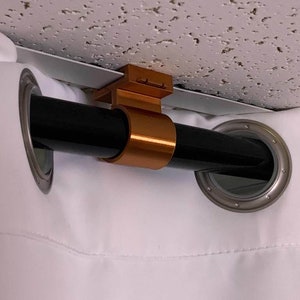 May include: A close-up of a black curtain rod with a gold metal bracket attached to a white ceiling. The rod is threaded through a white curtain with a silver grommet.