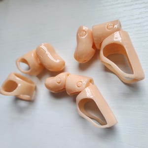 May include: Five plastic doll body parts in a peach color. The parts are for a doll's arms and legs. The parts are designed to be articulated.