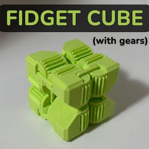 May include: A lime green fidget cube with gears, a puzzle toy. The text "FIDGET CUBE" is displayed above the cube in large, green letters, with the words "(with gears)" below. The cube is made of plastic and has a complex, interlocking design.