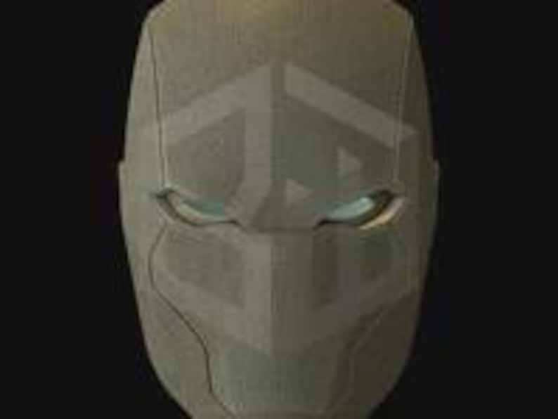 May include: A close-up of a gray, textured mask with a geometric design. The mask has eye openings with a subtle glow. The overall design is angular and modern, with a focus on clean lines and a futuristic aesthetic.