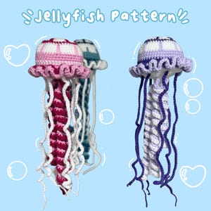 Pode incluir: Dois brinquedos de água-viva de crochê, um rosa e branco, o outro roxo e branco. Ambos têm longos tentáculos flutuantes.