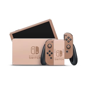 Könnte beinhalten: Eine roségoldene Nintendo Switch Konsole mit passenden Joy-Con Controllern. Die Konsole hat ein herzförmiges Design auf der Vorderseite mit dem Nintendo Switch Logo.