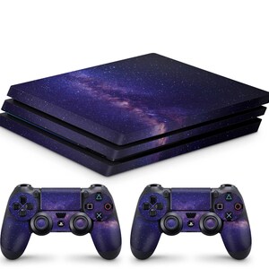 Könnte beinhalten: Eine schwarze PlayStation 4 Konsole mit einer Galaxie-bedruckten Haut. Die Konsole ist geschlossen und die Haut hat einen dunkelblauen Hintergrund mit weißen Sternen und einem hellblauen Nebel. Zwei passende Galaxie-bedruckte Controller sind enthalten.