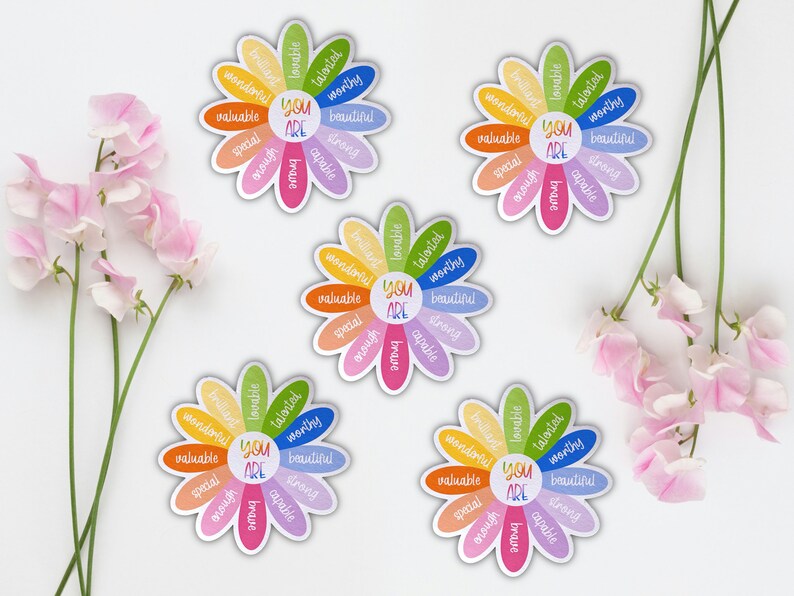 Pu&ograve; includere: Quattro carte di affermazione a forma di margherita colorate con il testo "You Are" al centro e affermazioni positive intorno ai petali. Le affermazioni includono "lovable", "talented", "worthy", "beautiful", "strong", "capable", "brave", "special", "enough", "valuable", e "wonderful".