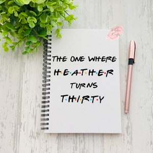 May include: White spiral notebook with the text "THE ONE WHERE HEATHER TURNS THIRTY" in black font with colourful dots between the letters. The text is styled to look like the title cards from the TV show Friends.