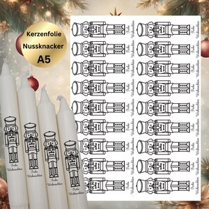 Könnte beinhalten: Weiße Kerzen und Aufkleberbögen mit einem schwarz-weißen Nussknacker-Design. Auf den Kerzen steht "Frohe Weihnachten". Der Aufkleberbogen hat mehrere Nussknacker-Bilder mit dem gleichen Text.
