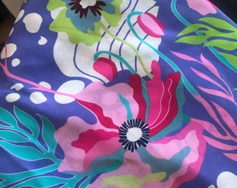May include: A purple fabric with a white background and a floral pattern. The flowers are pink, green, and blue. The fabric has a silky texture.