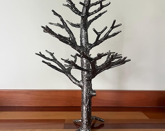 May include: A decorative metal tree sculpture with a textured, dark gray finish. The tree has a detailed trunk, branches, and a root-like base. The sculpture is designed to stand on a flat surface and adds a natural element to home decor.