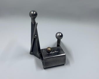 May include: A metal sculpture of two figures, one standing and one sitting, with a small gold ball in between them. The sculpture is made of welded metal and has a rustic, industrial look.