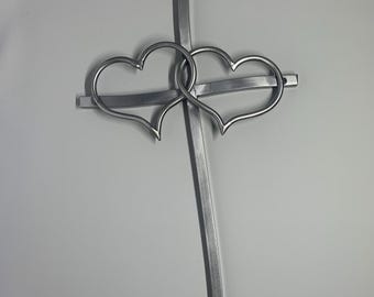 May include: A metal cross with two intertwined hearts. The cross is made of silver-colored metal and has a simple, elegant design. The hearts are connected at the center, symbolizing love and unity. The background is plain white.