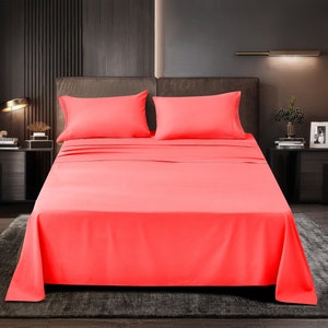 May include: A coral pink bed sheet set with two pillowcases. The bed is made with a fitted sheet and a flat sheet. The sheets are smooth and wrinkle-free.