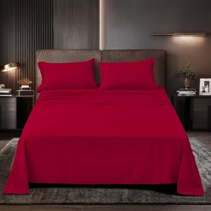 May include: A deep red fitted sheet with two matching pillowcases. The sheet is on a bed with a dark brown headboard and a dark brown nightstand.