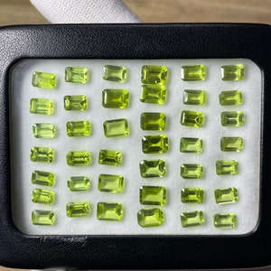 Può includere: Una collezione di 36 pietre preziose di peridoto verde in una teca nera. Le pietre preziose sono tutte tagliate a forma rettangolare e sono disposte in file.