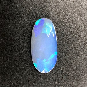 May include: A light blue oval opal gemstone with iridescent blue and green flashes.