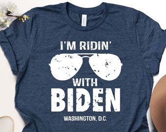May include: A navy blue t-shirt with a white graphic of sunglasses and the text "I'm Ridin' with Biden, Washington, D.C."